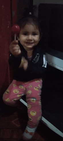 a little girl is holding a lollipop and wearing a black puma jacket