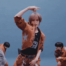 a man wearing a brown jacket and a black shirt with the letter f on it is dancing