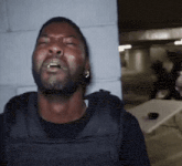 a man wearing a black vest is crying with his eyes closed and his mouth open .