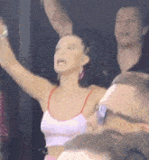 a woman in a pink tank top is raising her arms in the air in a crowd .