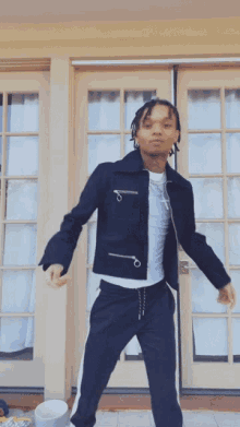 a young man in a black jacket and black pants is dancing in front of a door