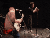 a man playing a guitar on a stage with another man singing into a microphone