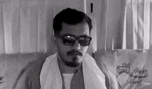 a man with a beard and mustache wearing sunglasses and a towel around his neck .