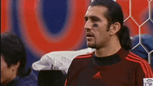a man wearing a red adidas jersey stands in front of a soccer goal
