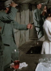 a group of people are standing around a table with a glass of red liquid