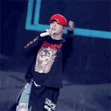 a man singing into a microphone wearing a red hat and a black shirt that says hip hop