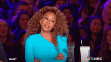 a woman in a blue dress stands in front of a crowd with a nbc logo on the bottom