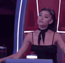 ariana grande is wearing a black dress and a black scarf around her neck while sitting in front of a table .