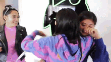 two girls are hugging each other in front of a neon sign . one girl is crying and the other is smiling .