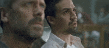 a man is sitting on a couch with his arms outstretched and another man is standing behind him .