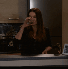 a woman in a black shirt is drinking from a glass