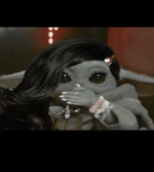 a baby yoda doll with long black hair and nails is covering her face .