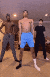 a shirtless man in blue shorts is dancing in a living room