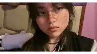 a girl with freckles on her face is taking a selfie while sitting on a bed .