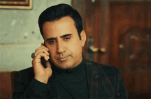 a man in a suit and turtleneck is talking on a cell phone