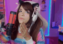 a woman wearing cat ears and headphones stands in front of a red microphone