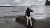a woman sits on a rock on the beach near the water