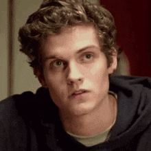 a young man with curly hair is wearing a blue hoodie .