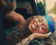 a woman wearing a blue head scarf is smiling and looking out of a car window