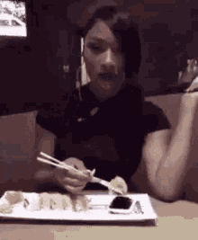 a woman is eating sushi with chopsticks at a table .