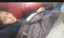 a woman in a jacket is laying on a bed with a red pillow