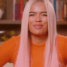 a woman with long pink hair is wearing an orange sweater and smiling .