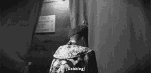 a black and white photo of a man standing behind a curtain with the words `` sobbing '' written on it .