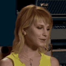 a close up of a woman wearing a yellow tank top and necklace .
