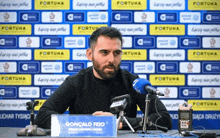 a man sitting in front of a microphone with a sign that says gonçalo feio