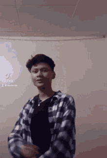 a young man wearing a plaid shirt and a black shirt is standing in a room .