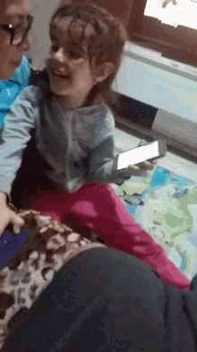 a little girl sitting on a woman 's lap holding a phone