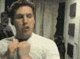 a man in a white shirt adjusts his tie in front of a mirror