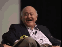 a man in a suit is laughing while sitting in a chair