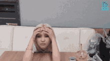 a woman is sitting at a table with her hands on her head ..