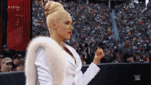 a woman in a white fur coat is standing in front of a crowd at a wrestling event .