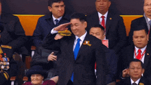 a man in a suit and blue tie salutes in front of a group of men