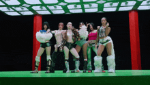 a group of women are standing on a green stage with a black background