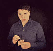 a man in a blue shirt is lighting a match with a matchbox in his right hand