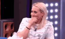 a woman with blonde hair is sitting on a couch with her hand on her face .