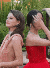 two women are standing next to each other one is wearing a red dress and the other is wearing a pink dress