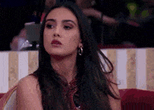 a woman with long dark hair is sitting on a couch and looking at the camera .