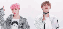two young men are standing next to each other and one has pink hair and the other has brown hair .