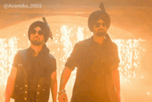 two men wearing turbans and sunglasses are standing in front of fire