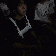 a group of young men are sitting in a dark room and one of them is wearing a shirt that says ' e '