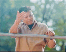 a man in a tan shirt is standing next to a metal railing