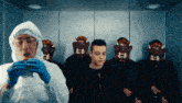 a man in a protective suit is eating a hamburger in front of a group of men wearing masks
