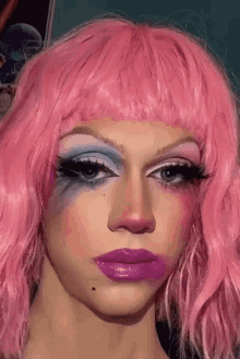a close up of a person wearing a pink wig and blue makeup .