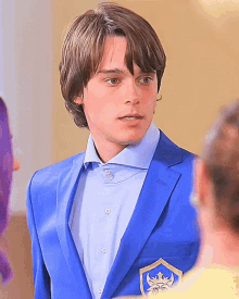 a young man in a blue suit has a gold emblem on his jacket pocket