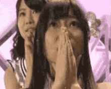 two women are covering their faces with their hands in front of a purple background .