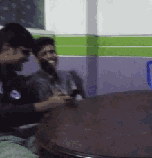 two men are sitting at a table and one is using a phone
